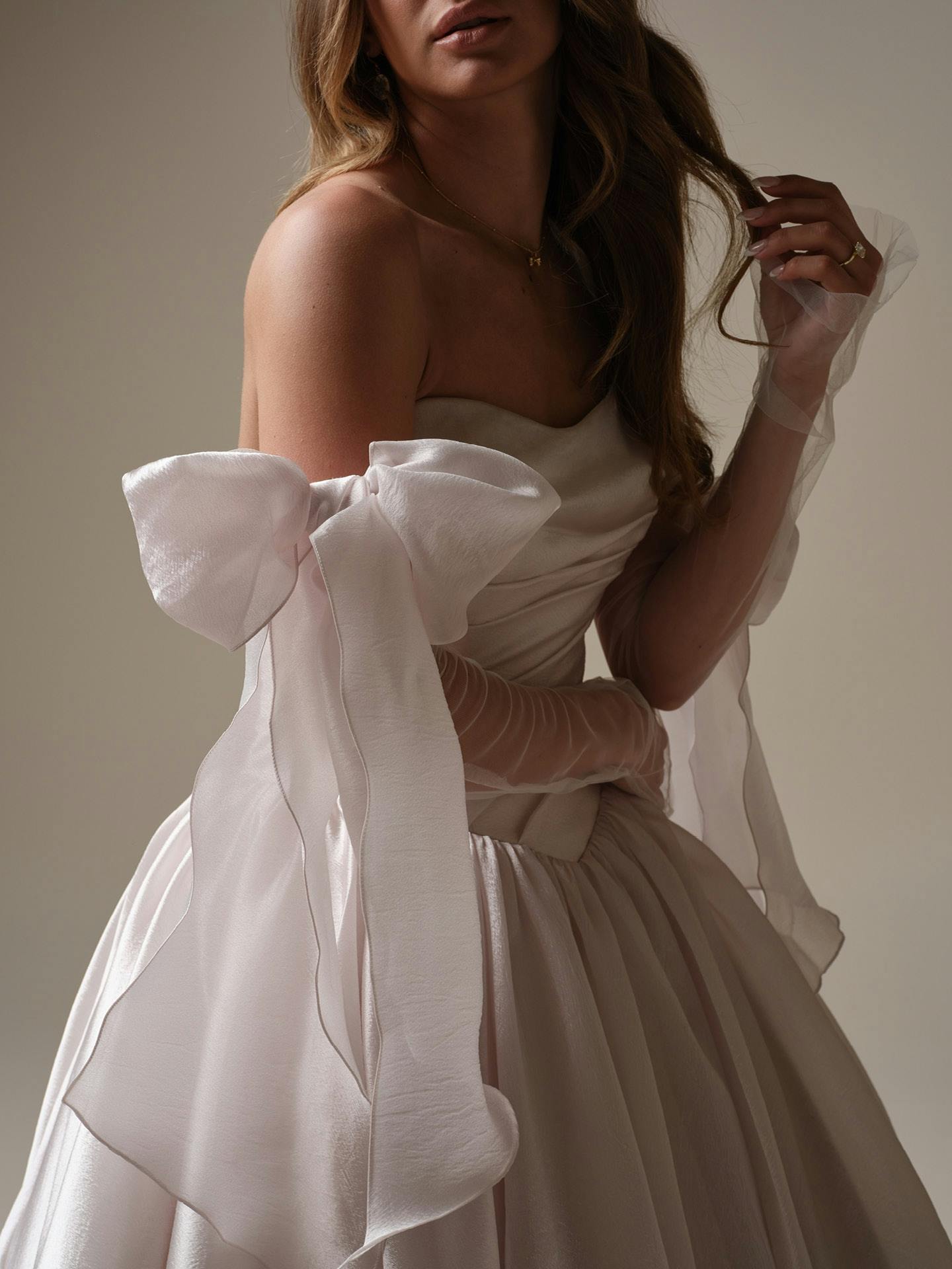 Woman wearing Paris by Maggie Sottero - a white wedding dress with a large bow detail against a neutral background