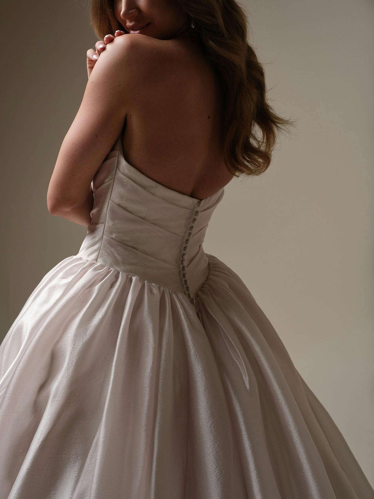 Woman wearing Paris by Maggie Sottero - a white strapless gown with a plain background