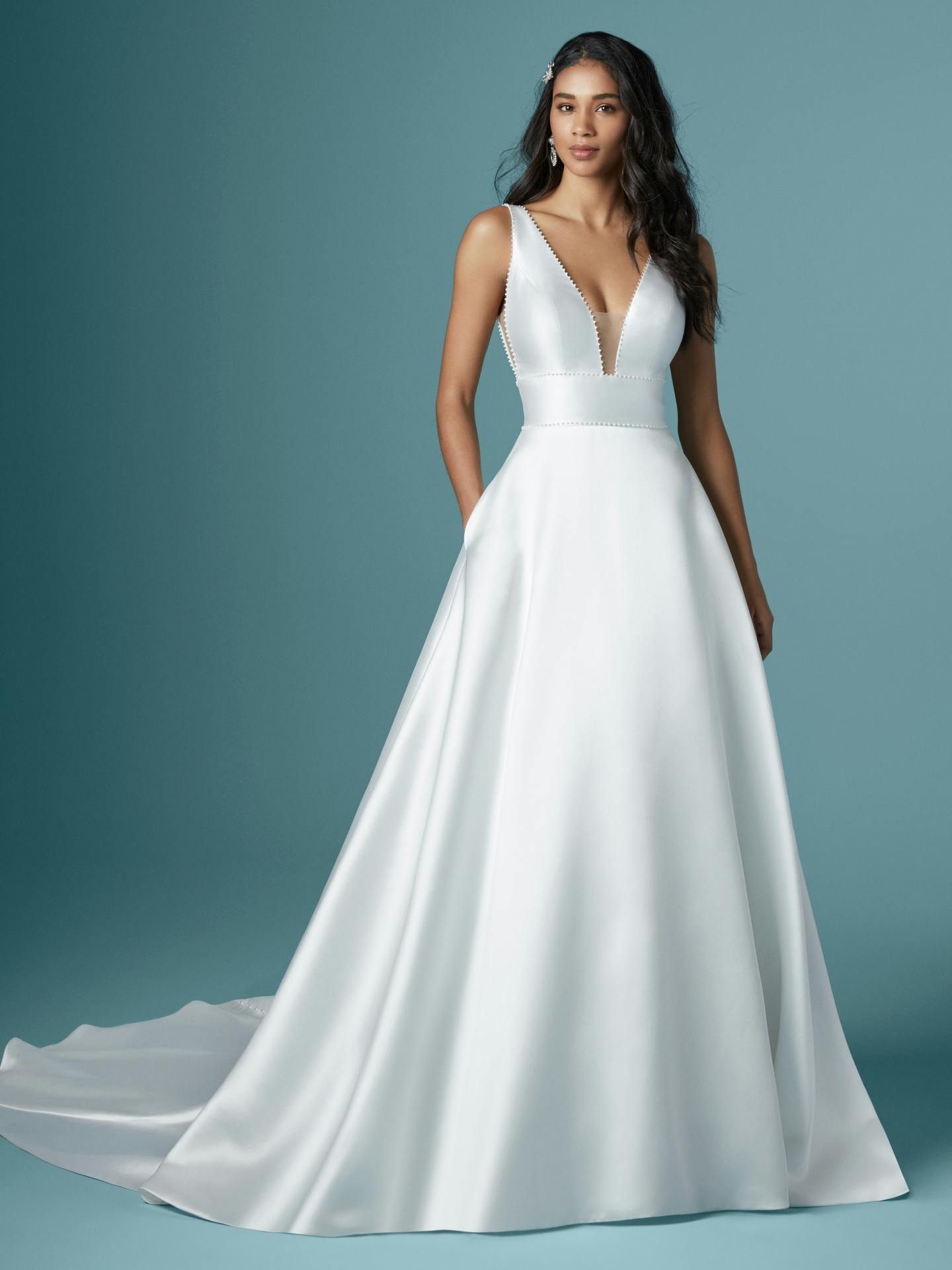 Woman wearing Raven by Maggie Sottero - a white wedding dress against a teal background