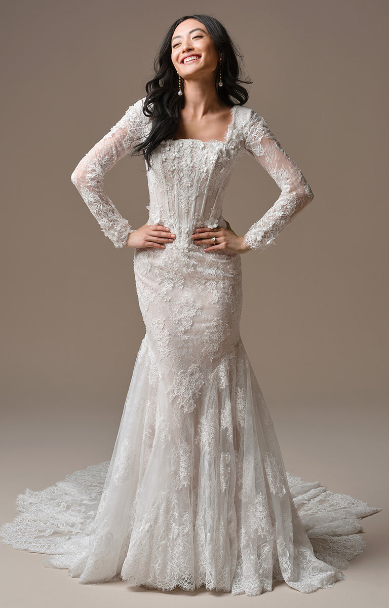 Woman wearing Takera Leigh by Maggie Sottero - Modest Fit-and-Flare Lace Wedding Dress with Illusion Sleeves with long sleeves against a neutral background