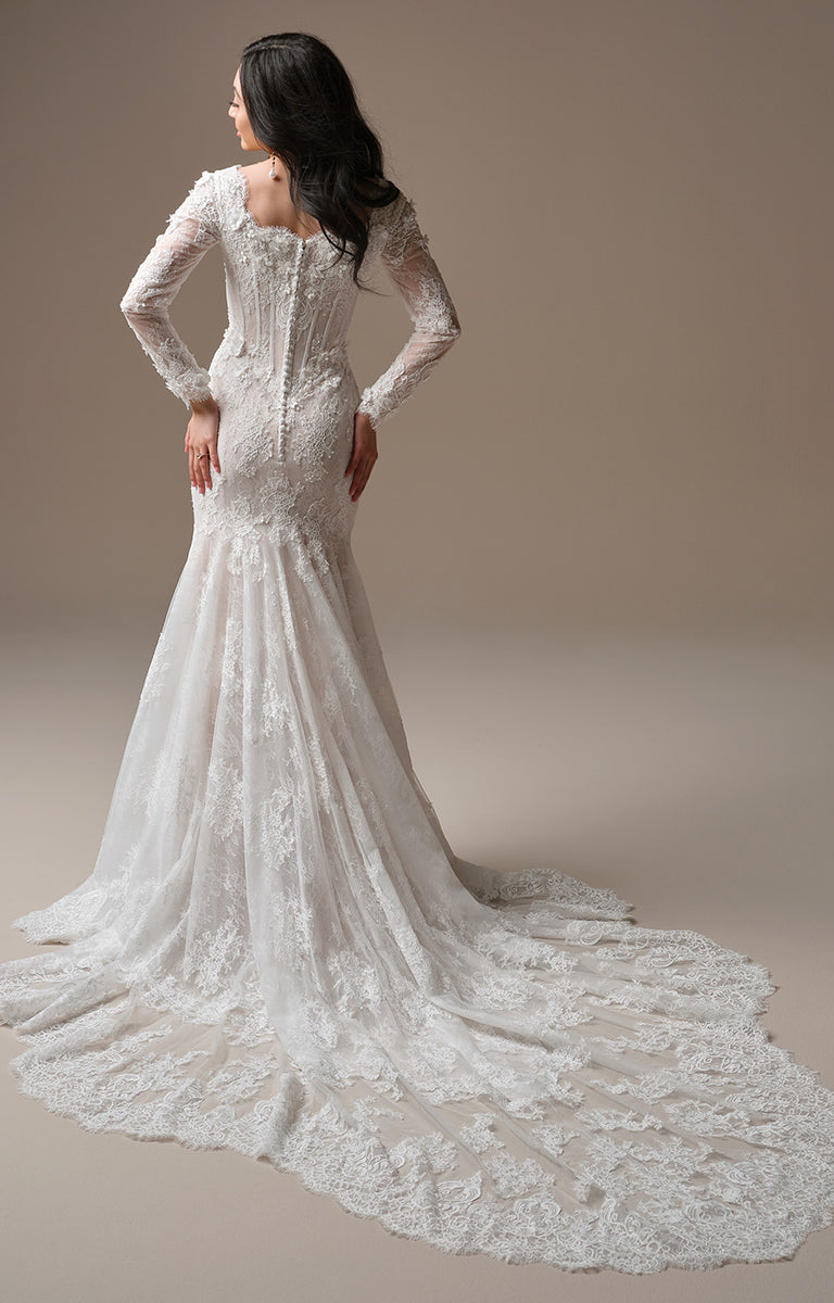 Woman wearing Takera Leigh by Maggie Sottero - Modest Fit-and-Flare Lace Wedding Dress with Illusion Sleeves with a long train on a plain background