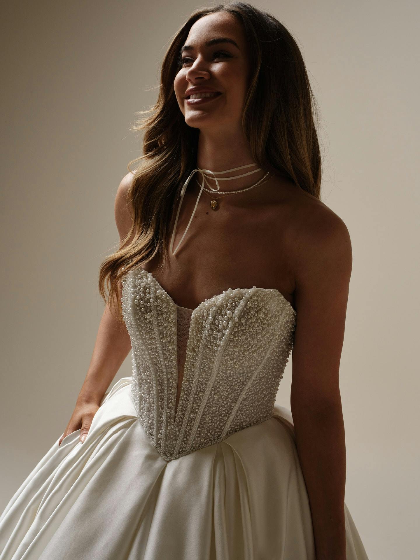 Woman wearing a strapless, beaded wedding dress against a neutral background