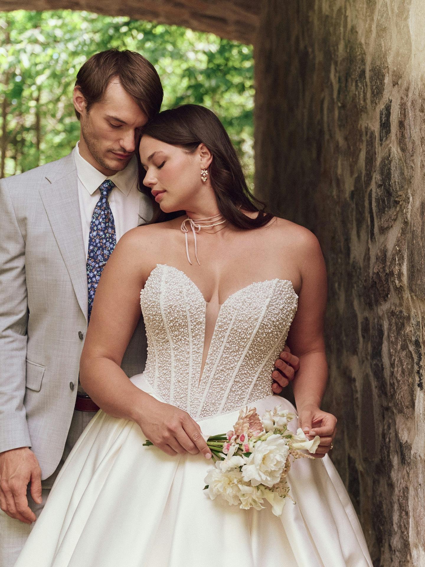 Man and woman in wedding attire standing close together outdoors.