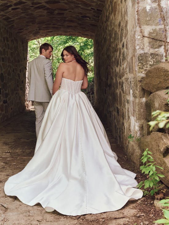 Woman in a white wedding dress standing under a stone archway with a man.