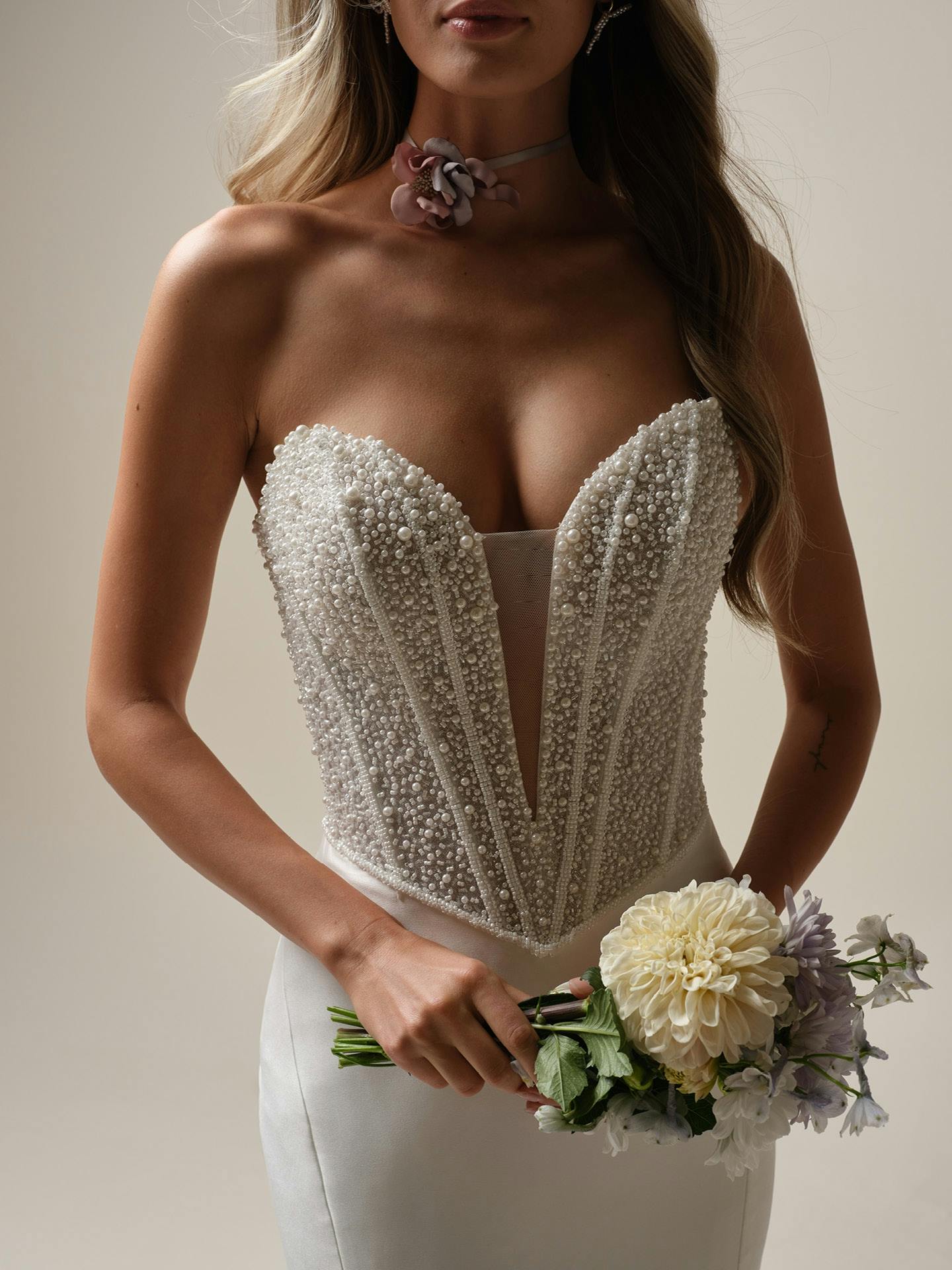 Woman wearing a strapless beaded wedding dress holding a bouquet of flowers.