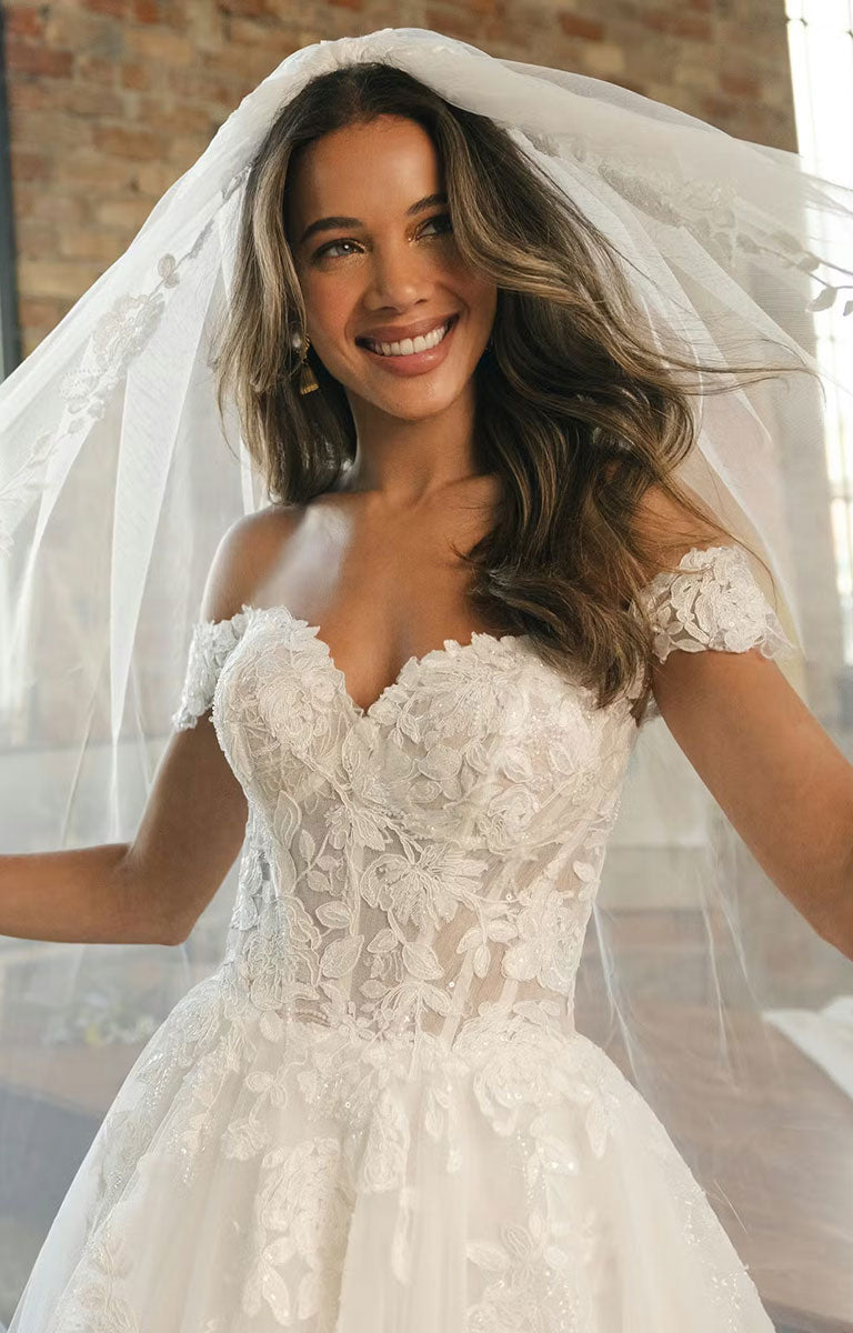 Woman wearing Verina Wedding Dress by Maggie Sottero - Off-the-Shoulder Lace A-Line Wedding Gown against a neutral background