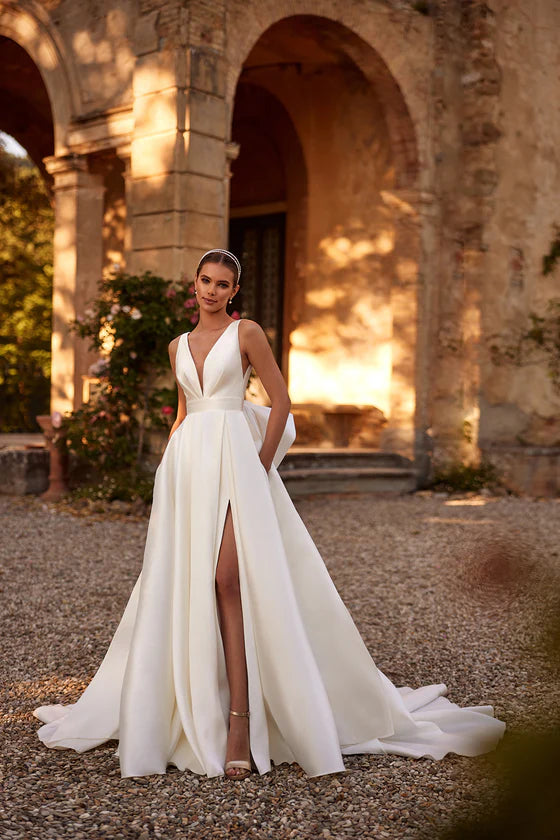 Woman in a white wedding dress standing in front of an old stone building with arches.