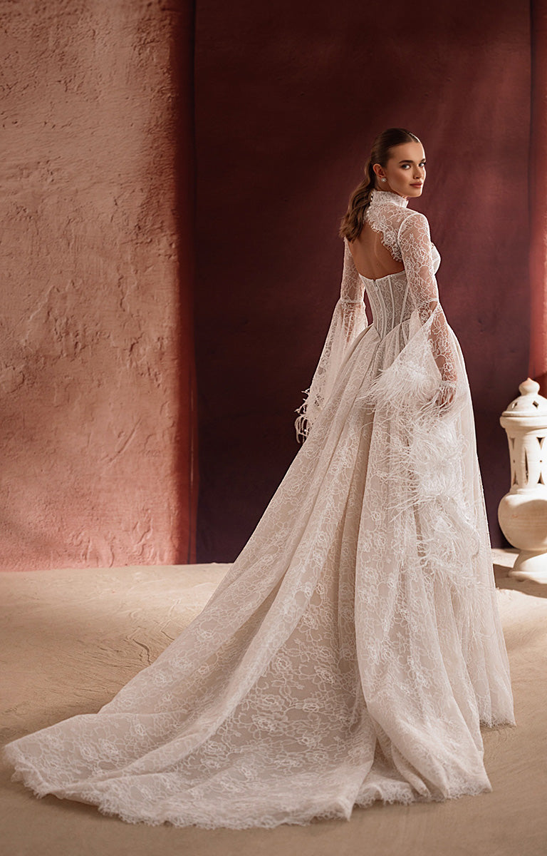 Woman in a lace wedding dress standing against a textured wall.