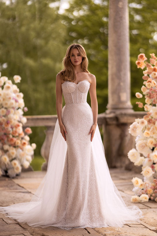 Woman in a white wedding dress standing in an outdoor setting with floral decorations.