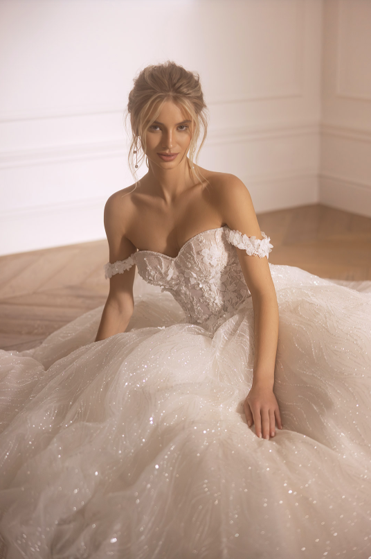 Woman in a sparkling wedding dress sitting on a bed.