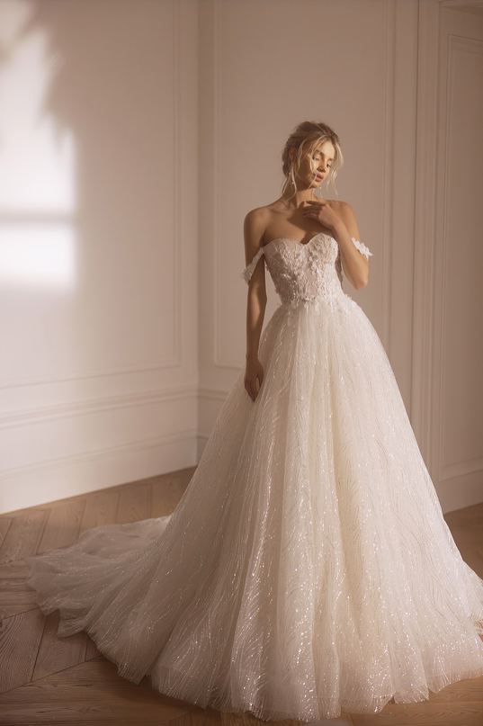 Woman in a white lace wedding dress standing in a softly lit room.