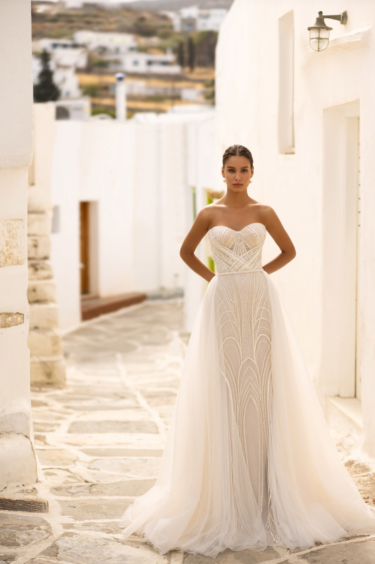 Woman in a white strapless wedding dress standing on a stone path with a scenic background.