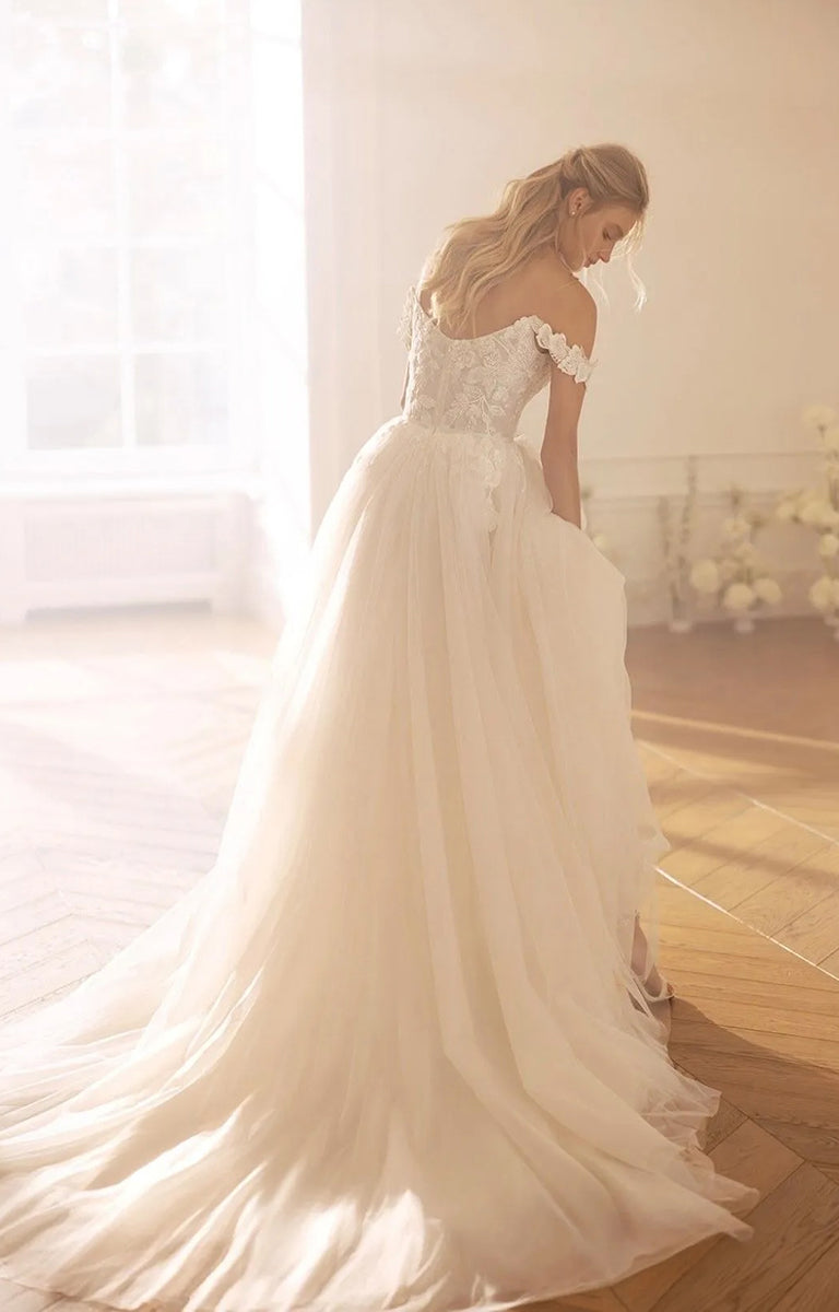 Woman in Ksenia by Monreal Bridal - Princess-Style Elegant Wedding Dress standing in a softly lit room.