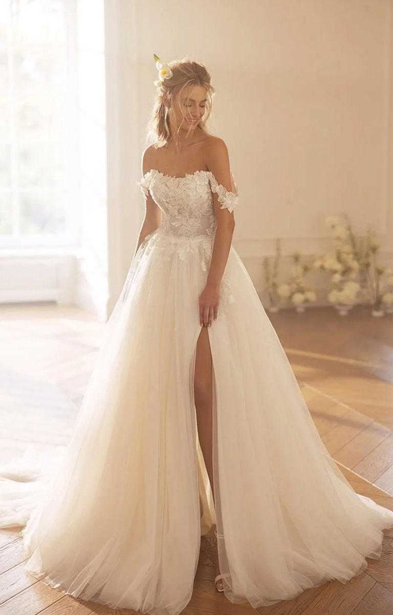 Woman in Ksenia by Monreal Bridal - Princess-Style Elegant Wedding Dress with a high slit standing in a softly lit room.
