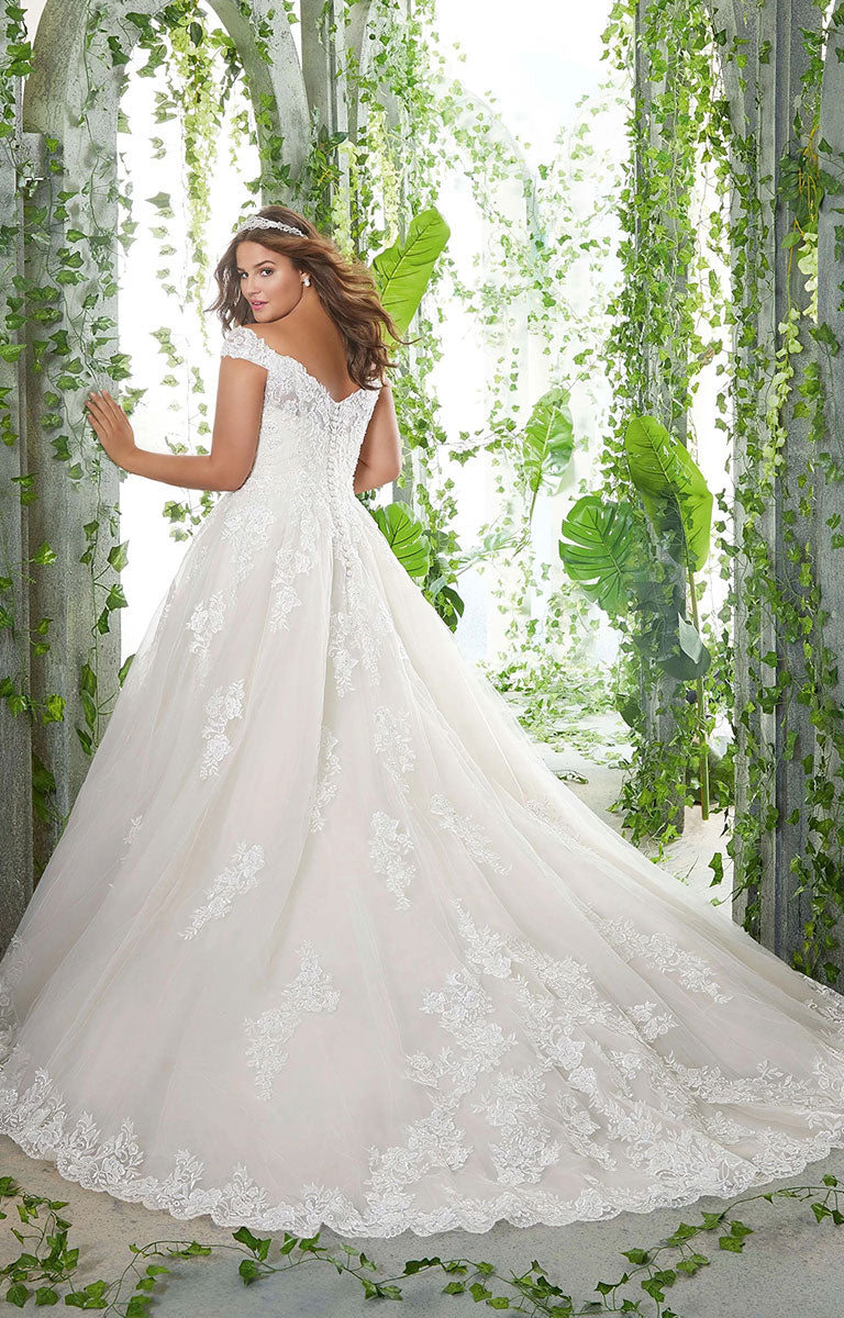 Woman in  Pamela Wedding Dress by Morilee Julietta - Plus Size Classic Ball Gown with Pearl and Crystal Beaded Lace Appliqués standing among greenery