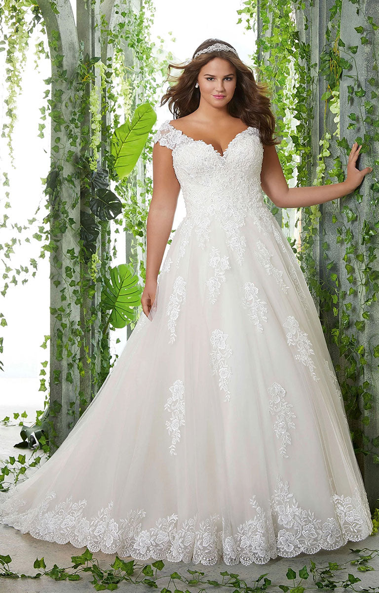 Woman in Pamela Wedding Dress by Morilee Julietta - Plus Size Classic Ball Gown with Pearl and Crystal Beaded Lace Appliqués standing in front of greenery
