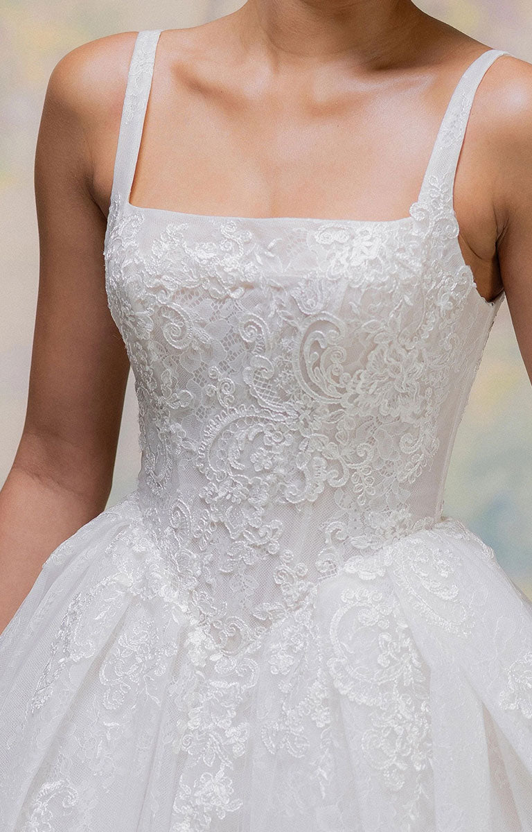 Close-up of Talis by Morilee - Lace Ball Gown Wedding Dress with Square Neckline, Basque Waist and Floral Appliqué with thin straps, a square neckline, and a full tulle skirt, shown on a model.