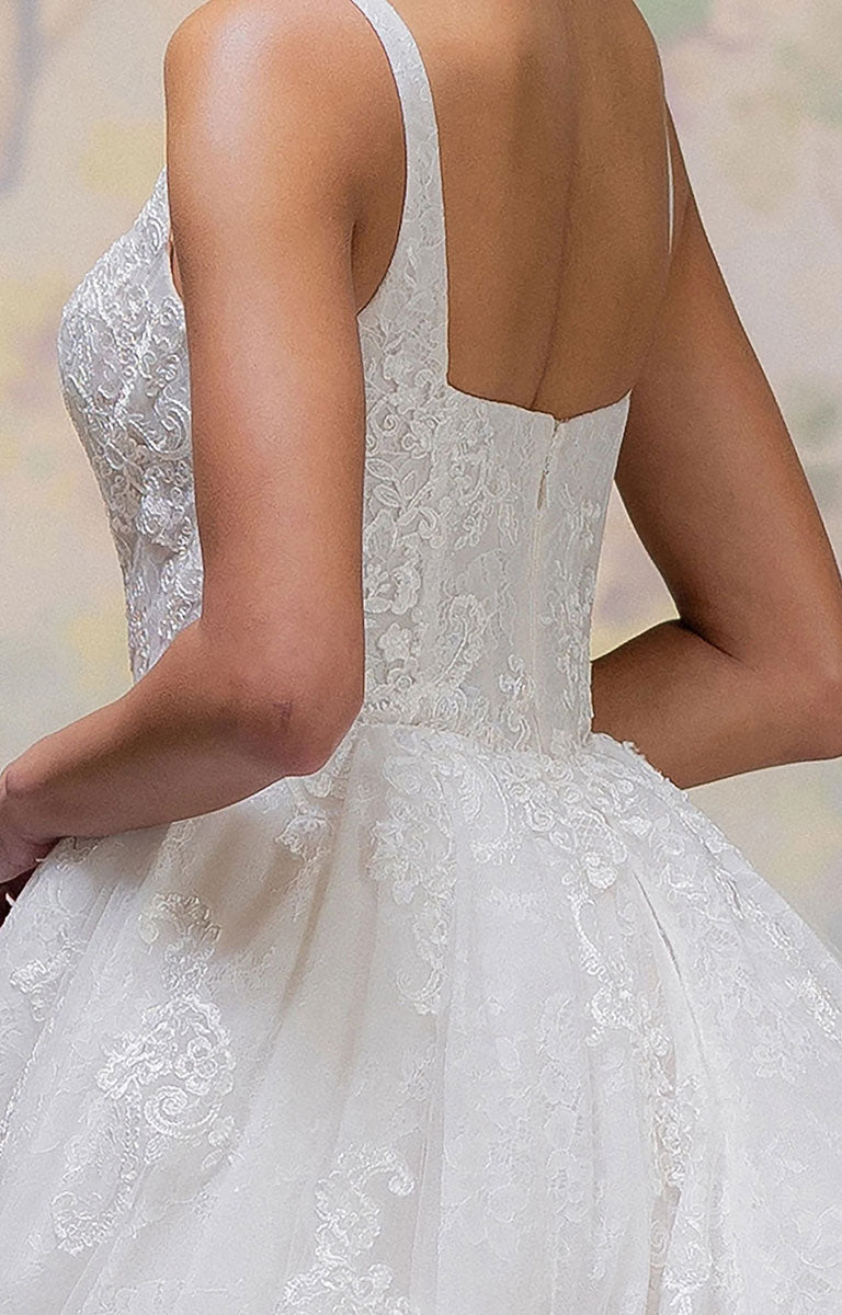 Close-up back view of a woman wearing Talis by Morilee - Lace Ball Gown Wedding Dress with Square Neckline, Basque Waist and Floral Appliqué with thin straps, a fitted lace bodice, and a full tulle skirt against a softly blurred neutral background.