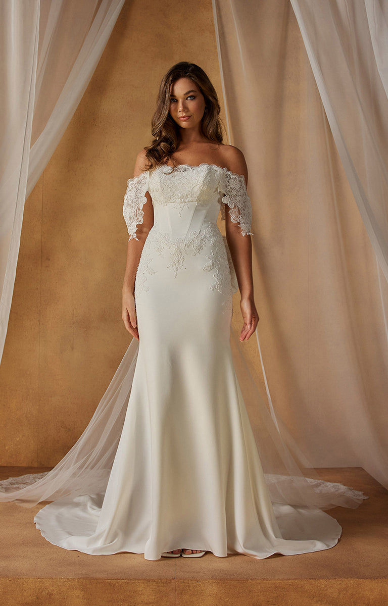 Woman wearing Natine ML26199 by Madi Lane - Fit-and-Flare Crepe Wedding Dress with Chantilly Lace Bodice with lace details against a beige curtain backdrop.