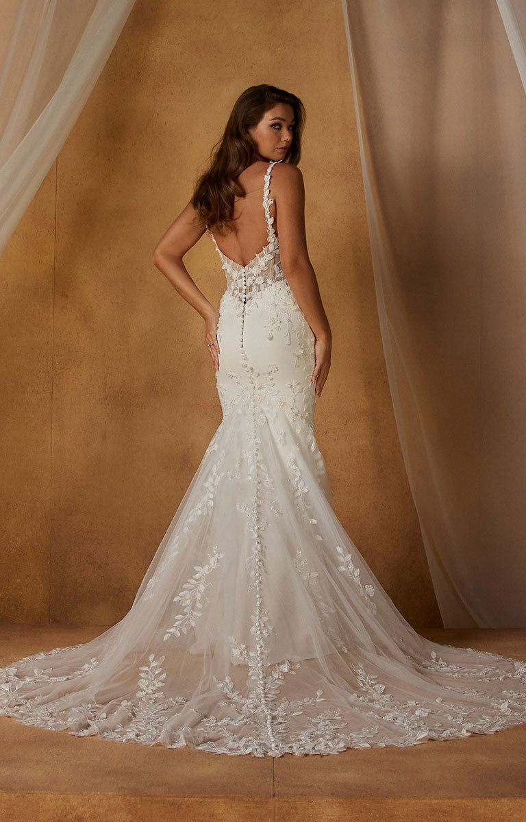A woman modeling Niall-Lee by Madi Lane - Fit-and-Flare Crepe Wedding Dress with Illusion Lace Bodice and Beaded Floral Straps from the back, standing in front of a warm brown backdrop with draped sheer fabric.