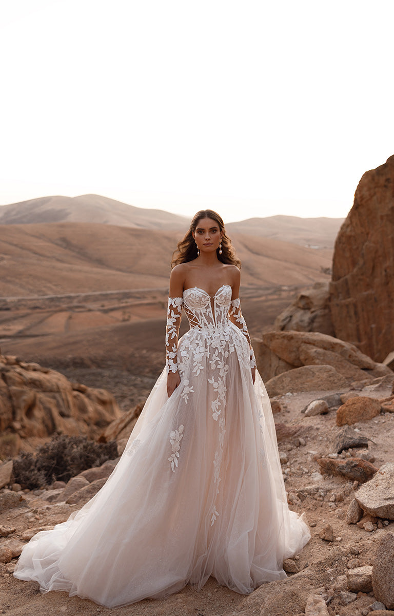 Woman in a white wedding dress with lace details standing in a desert landscape.
