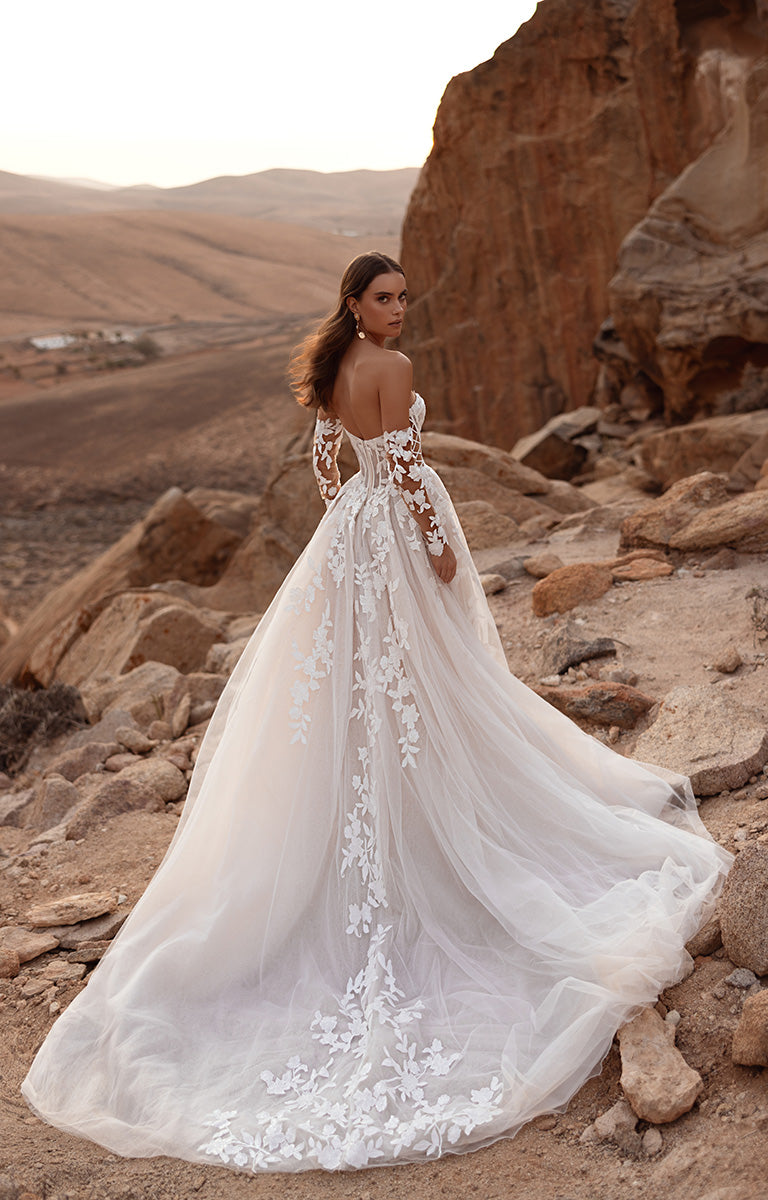 Woman in a white wedding dress with floral details standing on rocky terrain.