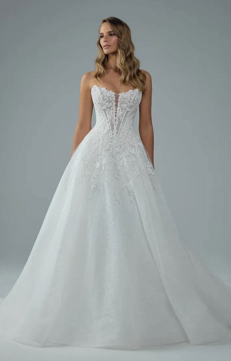 A woman modeling Neeve Y3237 by Sophia Tolli - Strapless Lace Ball Gown Wedding Dress with Glitter Tulle with a fitted lace bodice, sheer illusion center, and full tulle skirt against a light gray studio background.