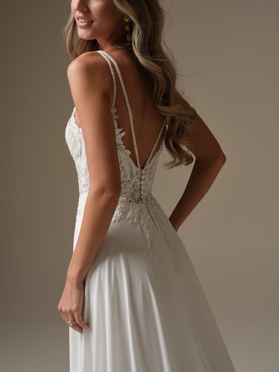 Woman wearing Avery by Rebecca Ingram - a white wedding dress with intricate back design on a neutral background