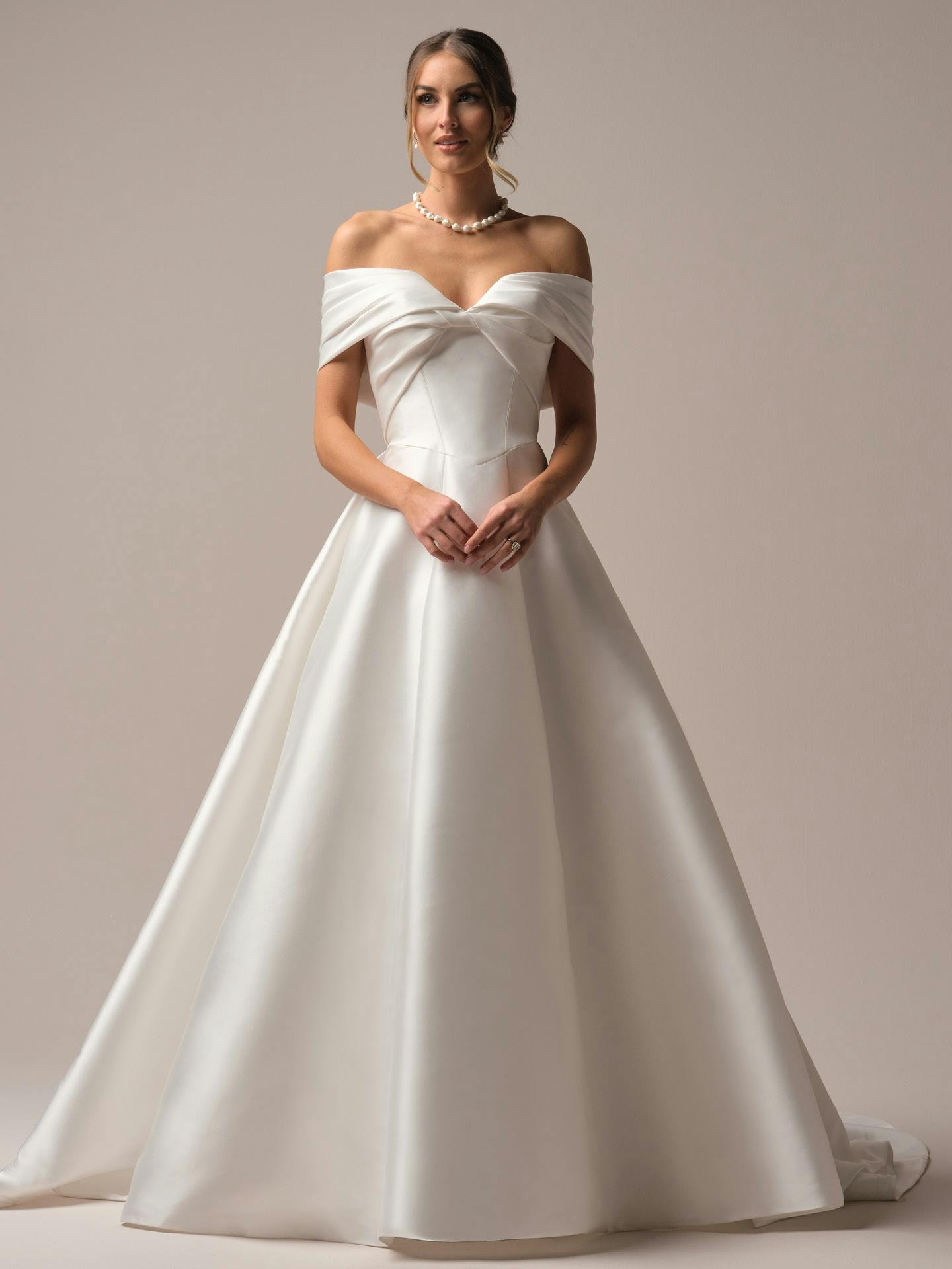 Woman wearing a white off-shoulder wedding dress against a plain background