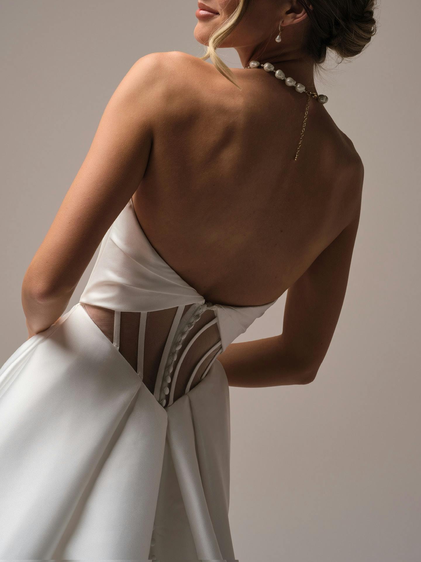 Woman wearing a white dress with a backless design and embellishments on a neutral background