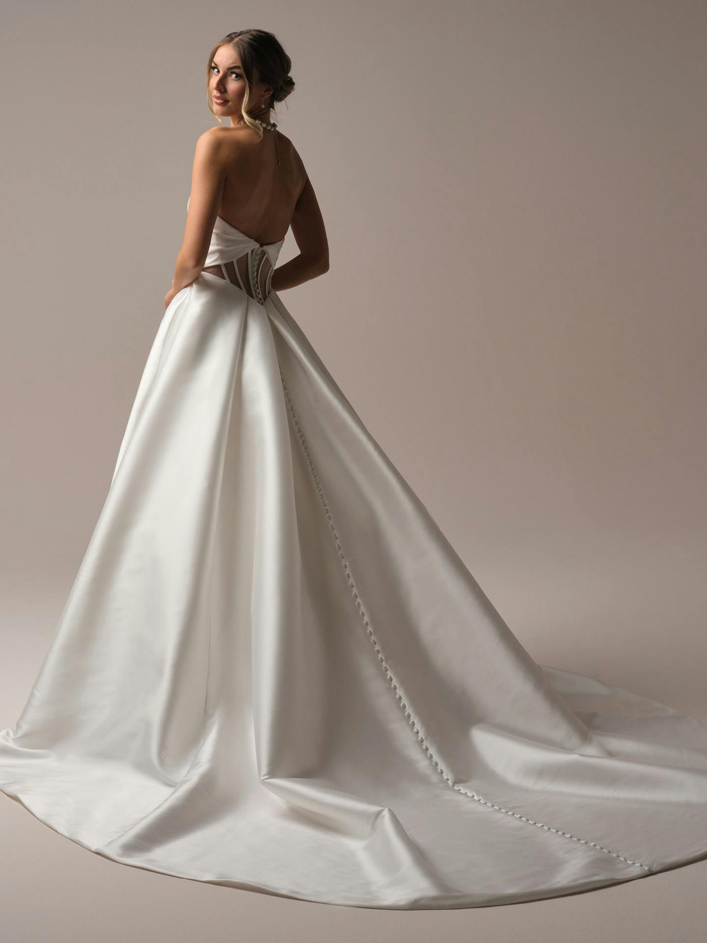 Woman wearing a white wedding dress with a long train on a plain background