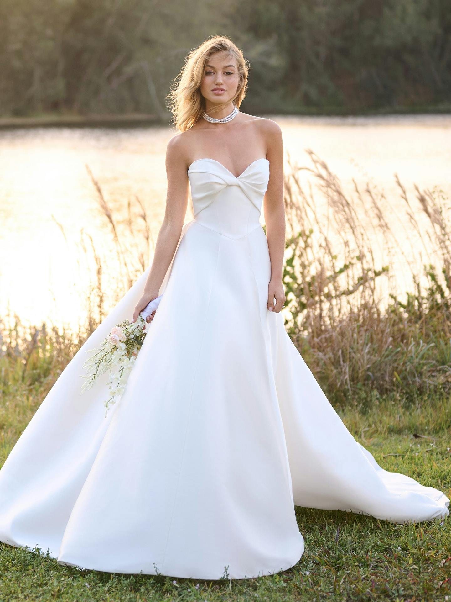 Woman in a strapless white wedding dress standing outdoors with a blurred natural background