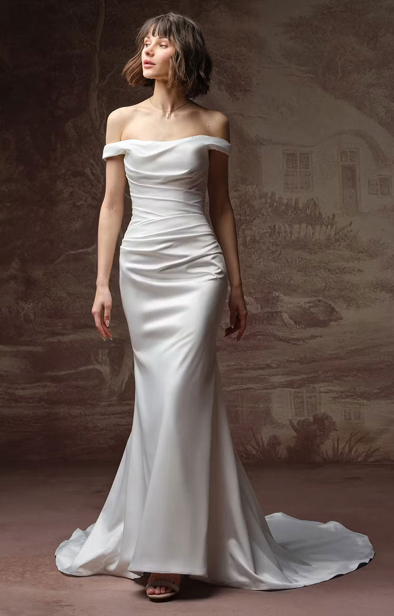 Clementine by Rebecca Ingram - Sculpted Fit-and-Flare Satin Wedding Dress with Draped Off-the-Shoulder Sleeves with a draped bodice and a long train, worn by a model standing against a sepia-toned scenic backdrop.