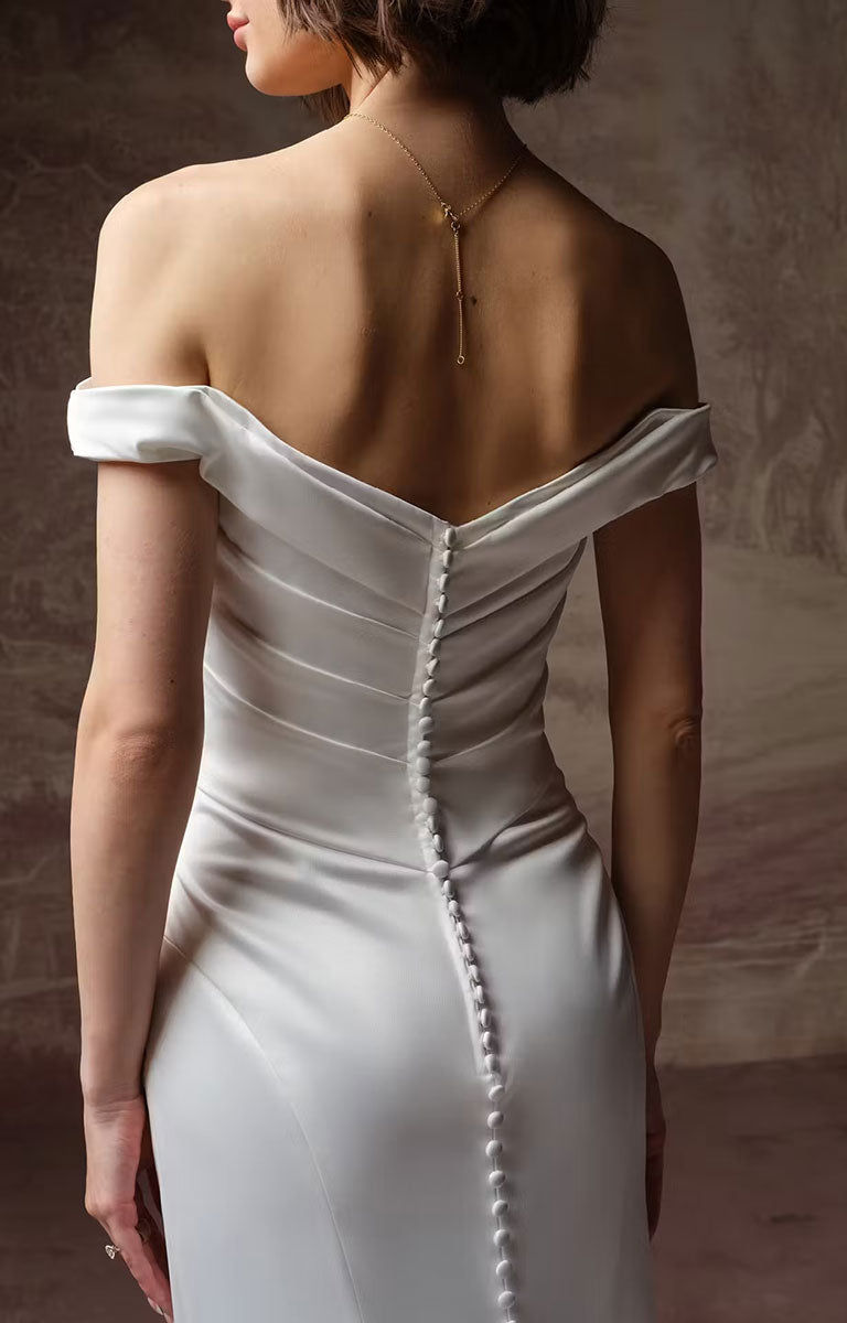 A woman wearing Clementine by Rebecca Ingram - Sculpted Fit-and-Flare Satin Wedding Dress with Draped Off-the-Shoulder Sleeves showcasing the rear of the dress with covered buttons. 