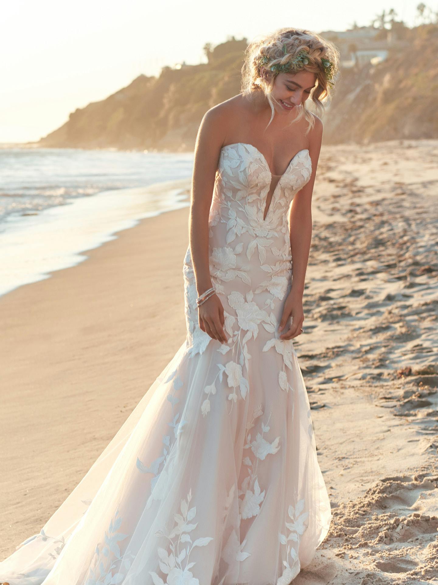 Woman in Hattie by Rebecca Ingram - a strapless floral wedding dress on a beach