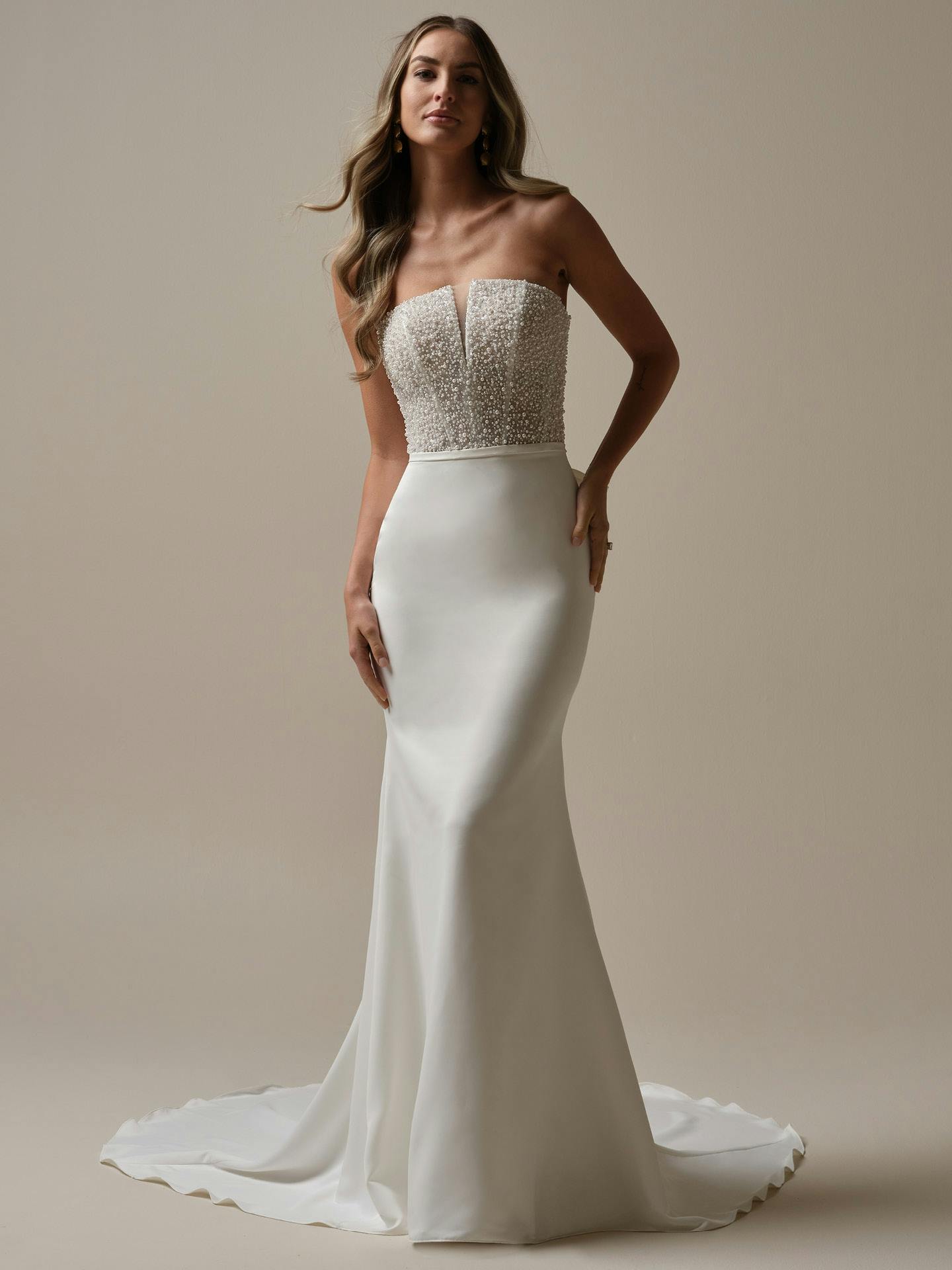 Woman wearing a strapless wedding dress with beaded top and plain skirt on a beige background