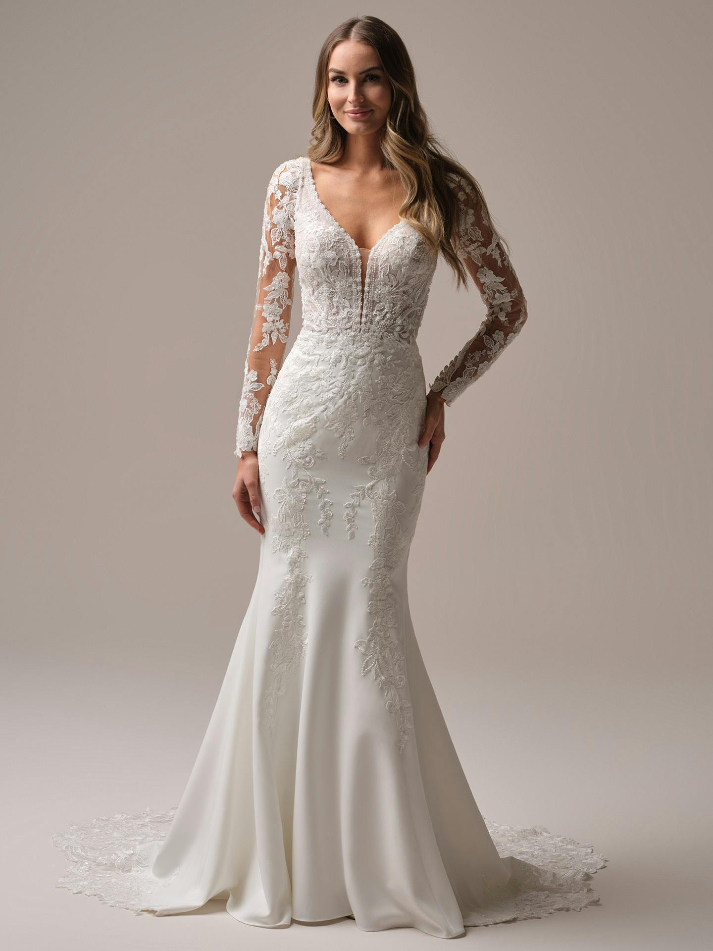 Woman wearing a white lace wedding dress with long sleeves on a plain background