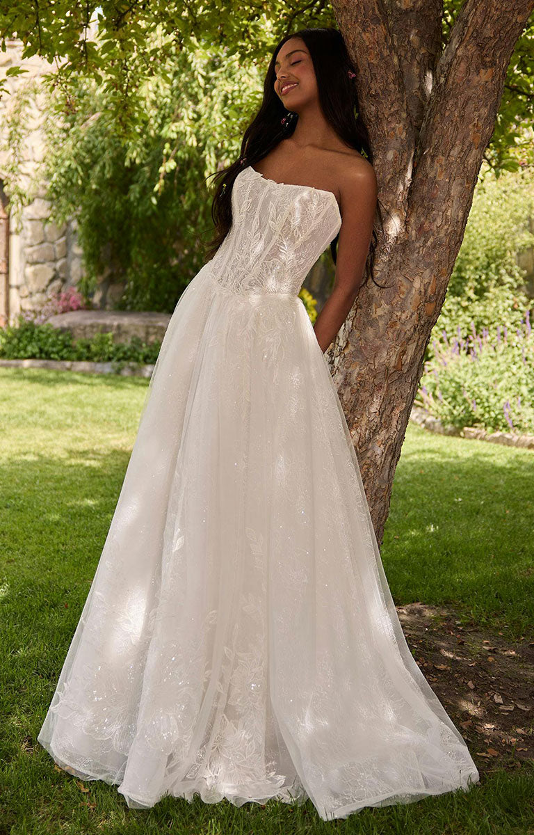 Woman in Lisa by Rebecca Ingram - Cat Eye Neckline Illusion Lace Ballgown Wedding Dress standing next to a tree in a garden setting