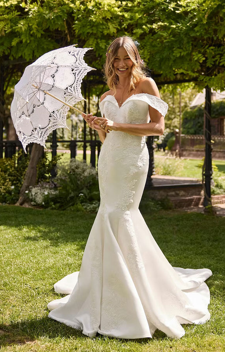 Woman in Miley by Rebecca Ingram - Off-the-Shoulder Fit-and-Flare Wedding Dress with Sequined Lace Accents holding a lace parasol in a garden setting