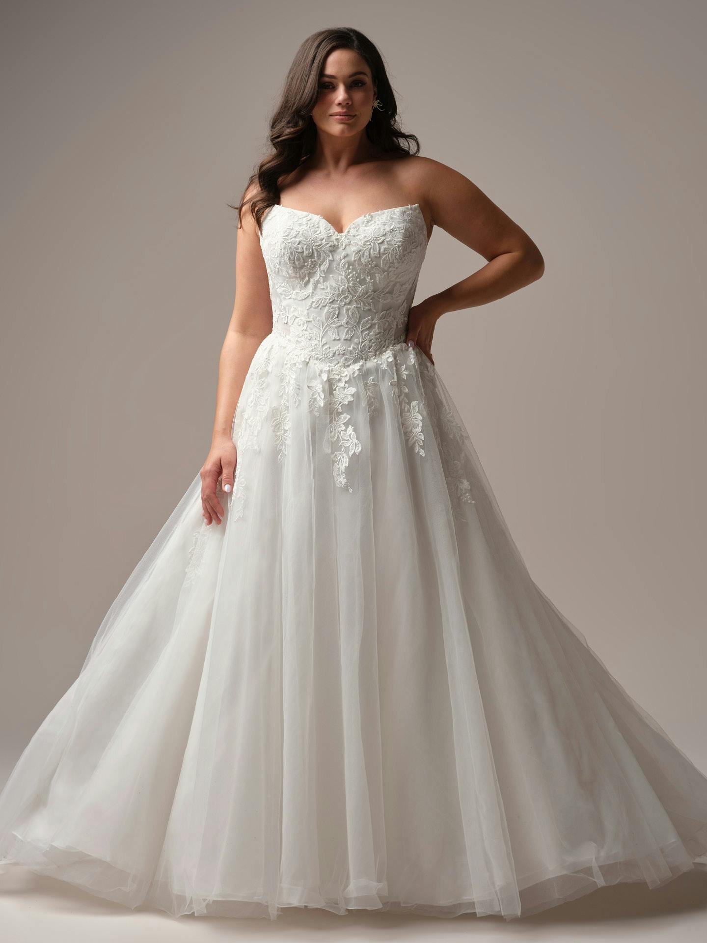 Woman wearing a white wedding dress with lace bodice and flowing skirt on a plain background