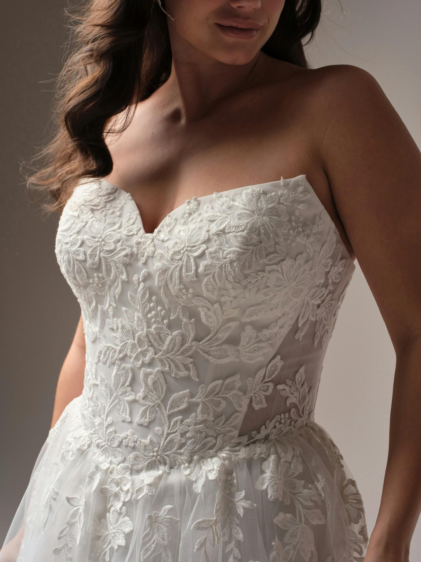Close-up of Paige by Rebecca Ingram - a strapless lace wedding dress with a neutral background