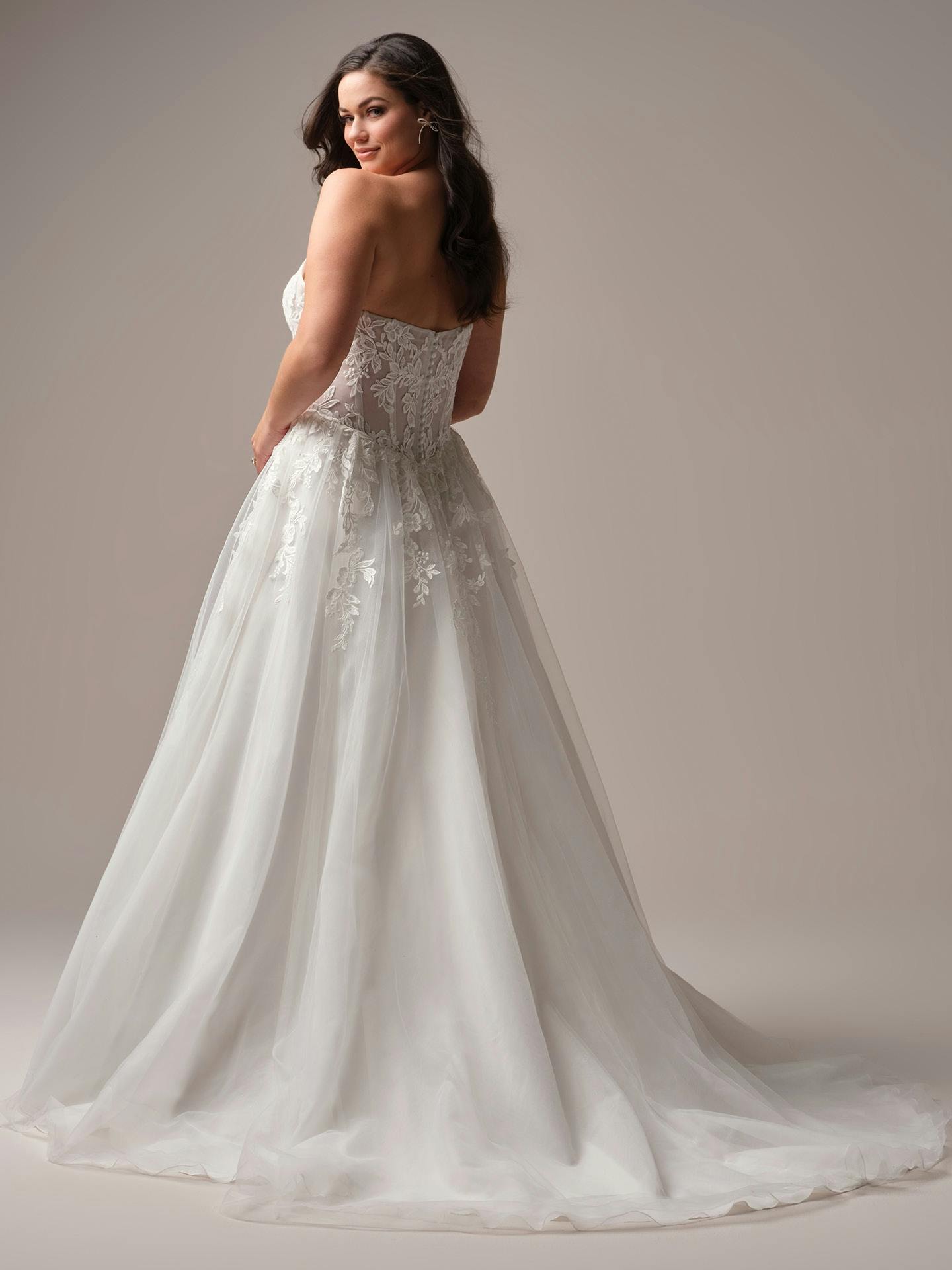 Woman wearing Paige by Rebecca Ingram - a white wedding dress with intricate detailing on a plain background