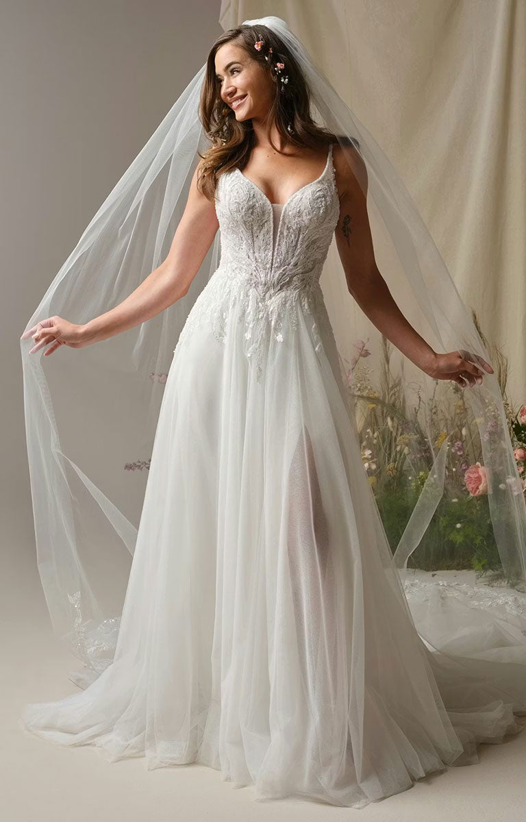 Woman in Valarie by Rebecca Ingram - Sparkle Lace A-Line Wedding Dress with Plunging V-Neck and Side Slit against a neutral background