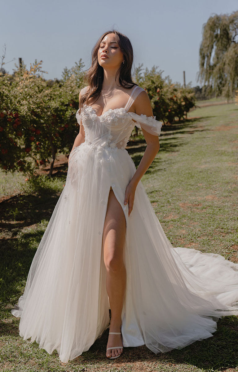Woman in a white wedding dress standing outdoors with greenery in the background