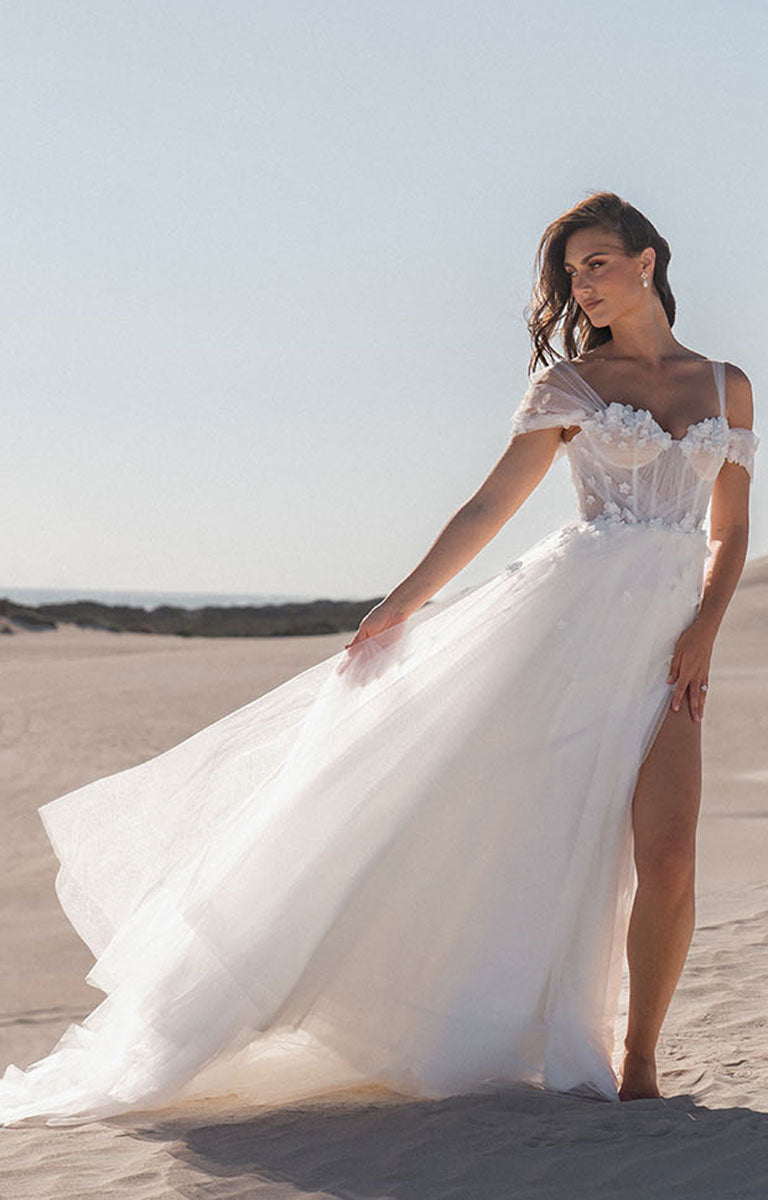 Woman in a white wedding dress standing on a sandy beach.