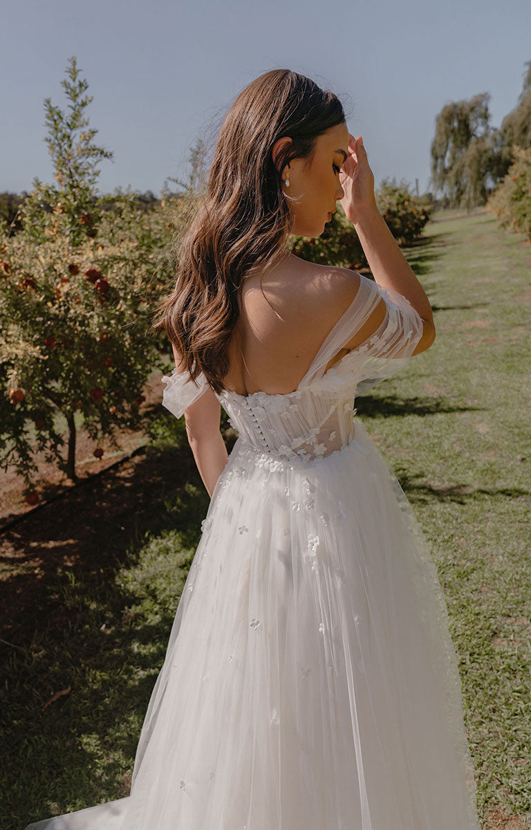 Woman in a white wedding dress standing in a natural setting with trees and grass.