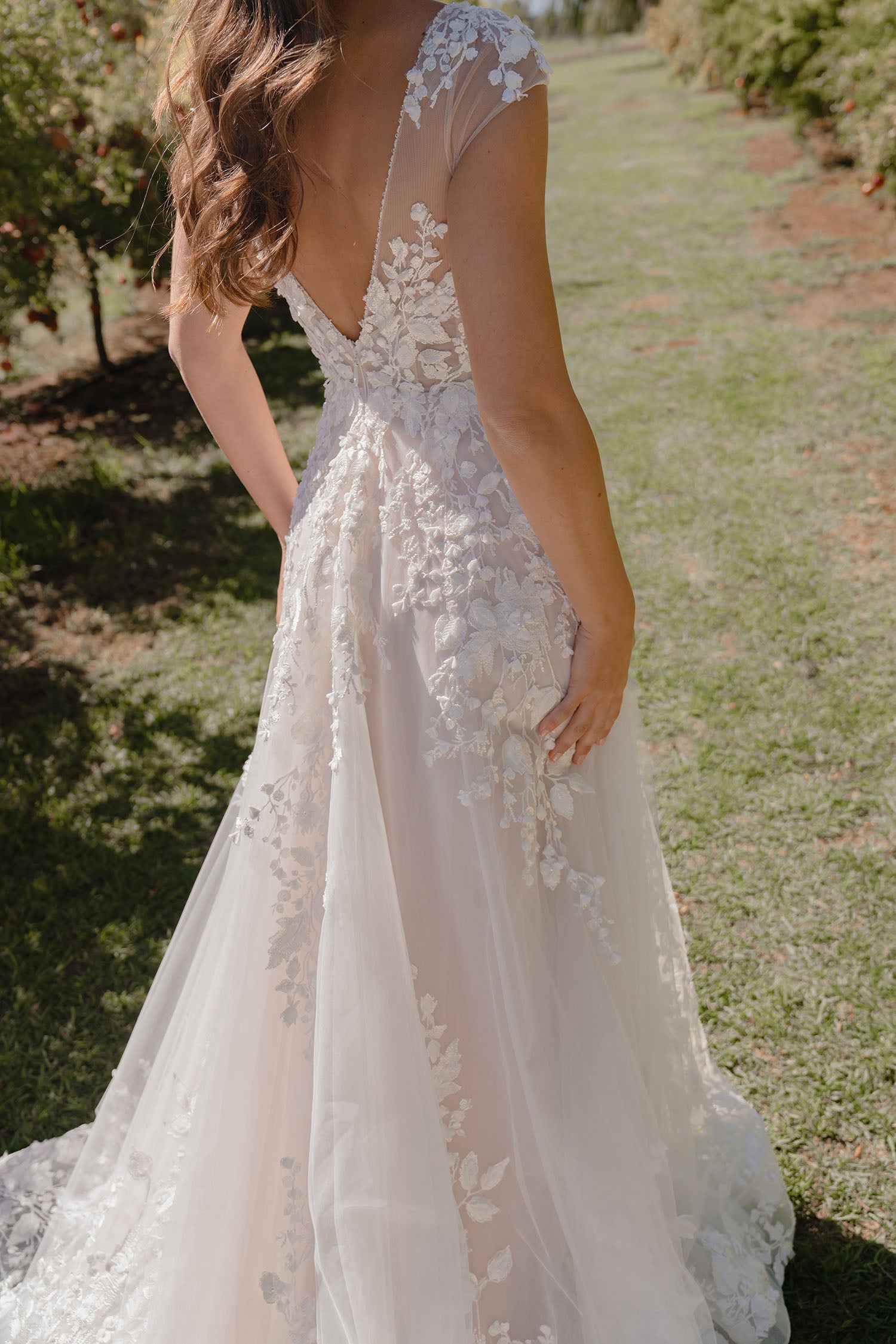 Woman wearing Sarah by Madi Lane, a white lace wedding dress in an outdoor setting