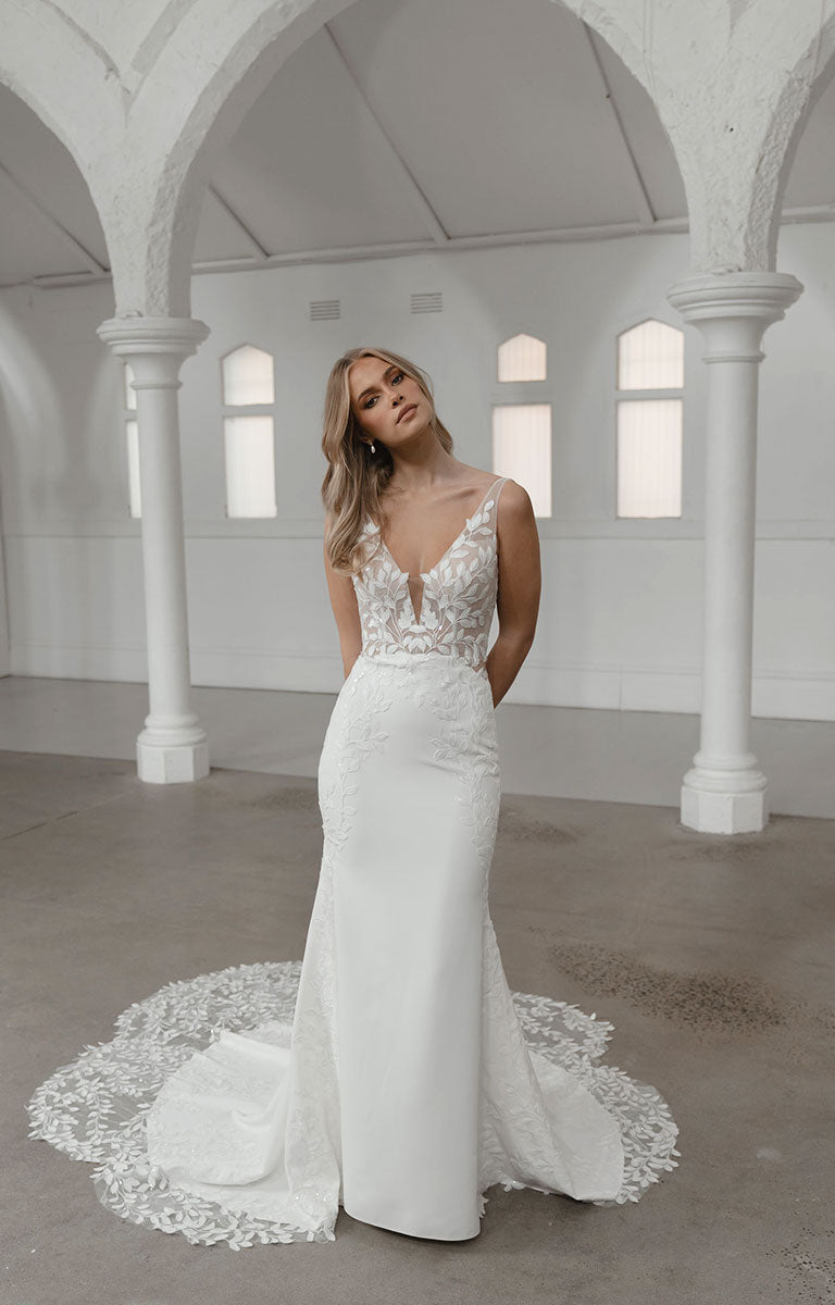 Woman in a white wedding dress standing in a spacious room with high ceilings and large windows.