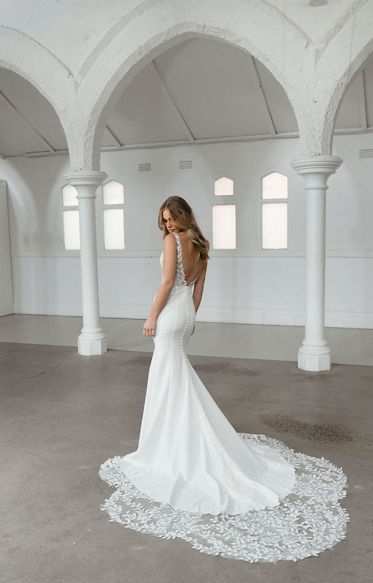 Woman in a white wedding dress with a lace train in a spacious, architecturally interesting room.