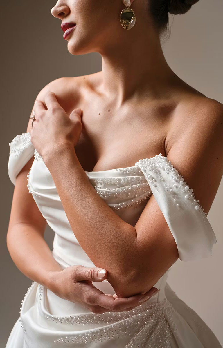 Woman wearing Kincaid by Sottero and Midgley - Ruched Satin Ballgown Wedding Dress with Pearl Details and Cat-Eye Neckline with intricate detailing on a neutral background